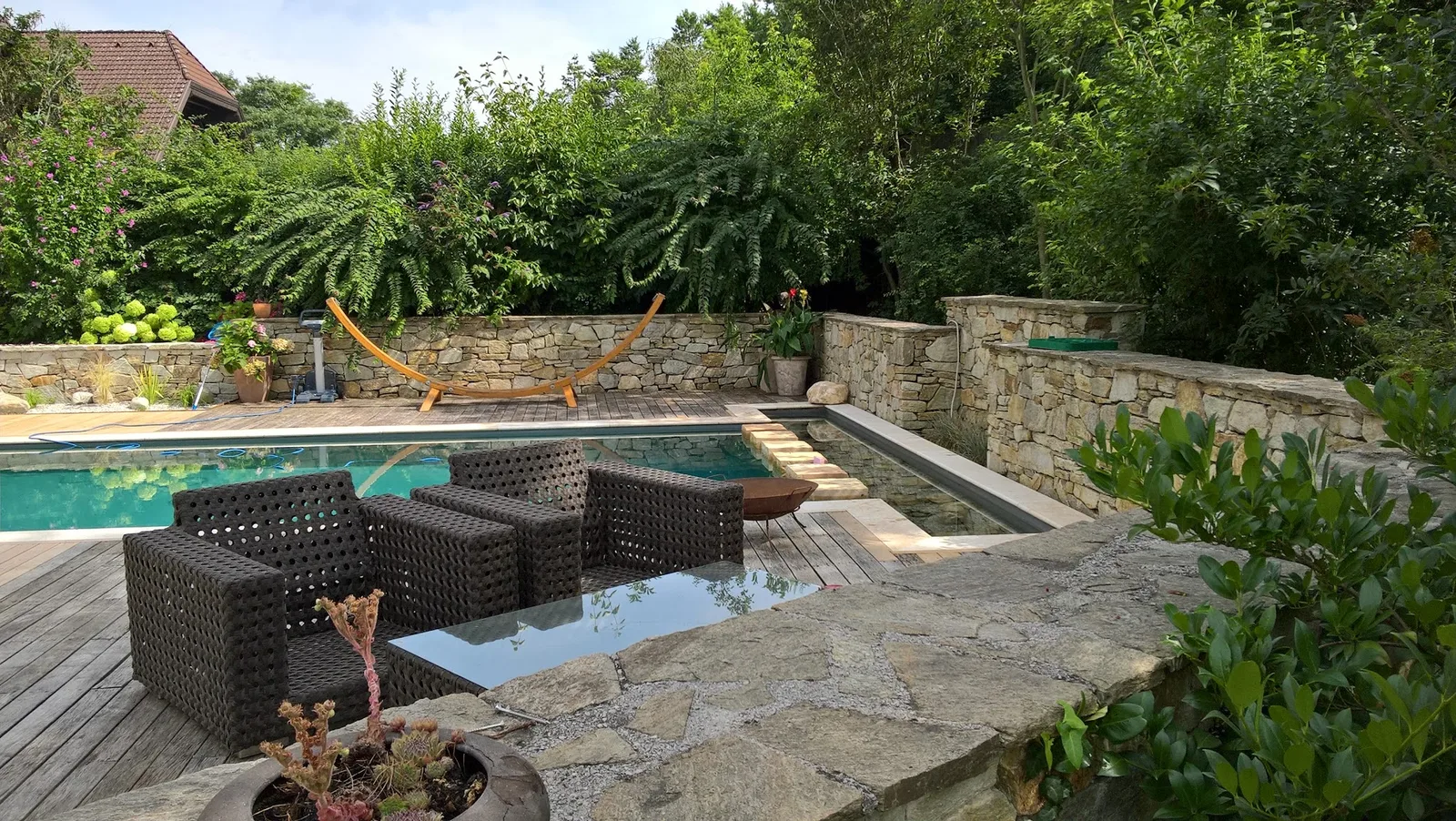 Poolterrasse mit Holzdeck, Natursteinmauern und Sitzmöbeln